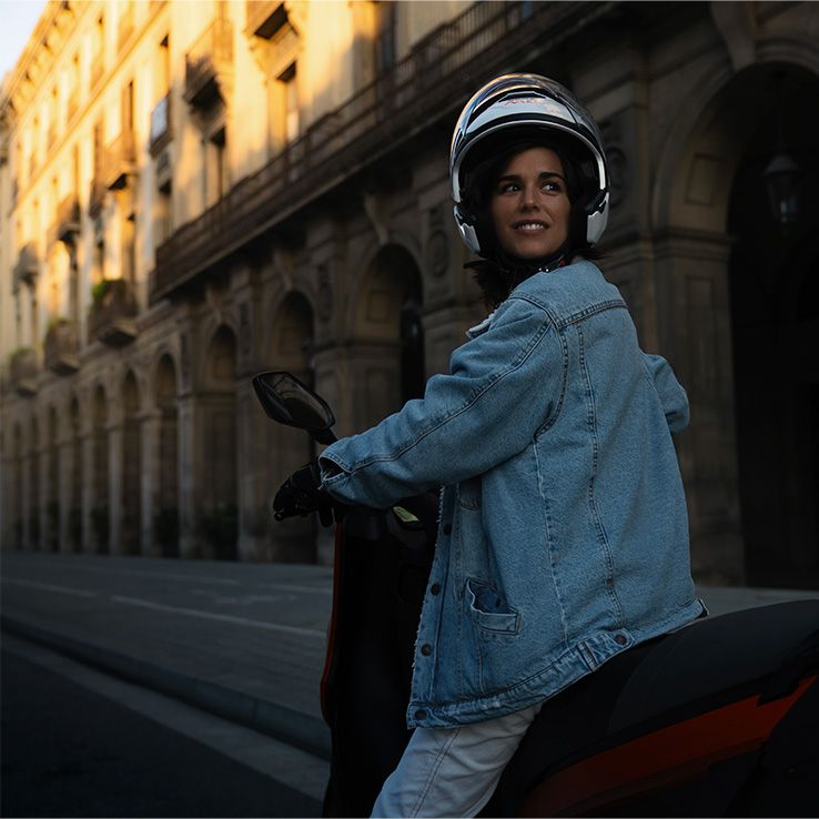 Eine Frau mit Helm sitzt auf einem SEAT Mo 125 und blickt zurück.