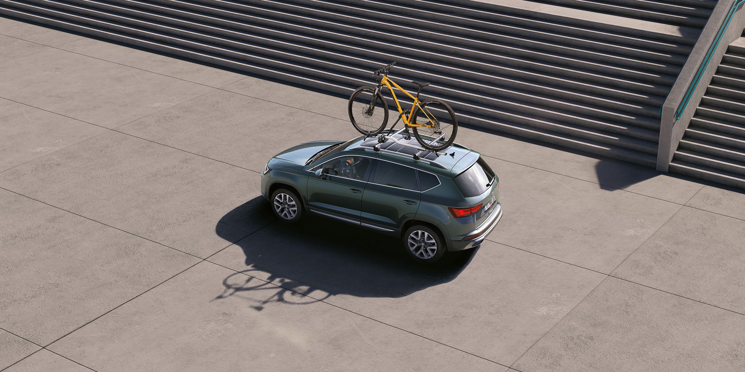 Ein grüner SEAT Ateca mit Fahrraddachträger und Fahrrad auf dem Dach.