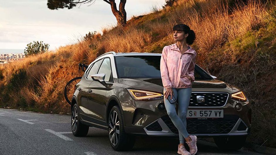 Eine Frau lehnt an der Motorhaube eines SEAT Arona.