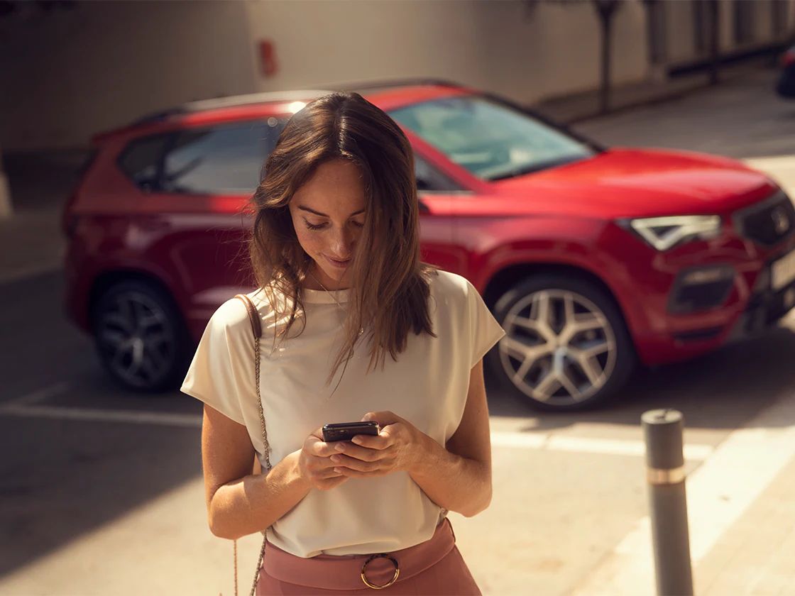 Frau verlässt ihr Auto und schaut auf ihr Handy  mit SEAT CONNECT