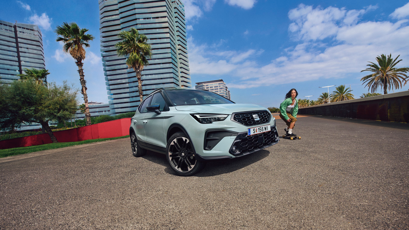 SEAT Arona zwischen Palmen mit Mädchen auf Skateboard rechts daneben