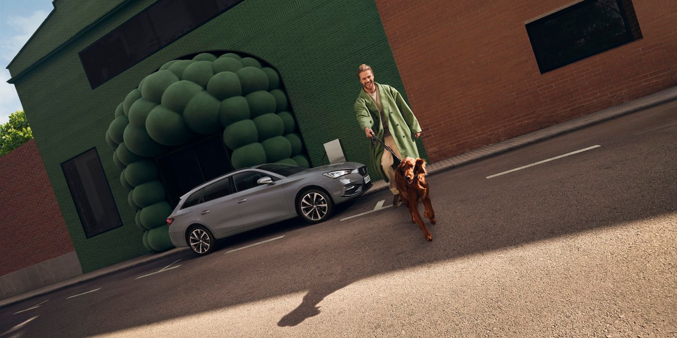 Seitliche Ansicht eines grauen SEAT Leon SP Kombi, ein Mann mit Hund befindet sich rechts neben dem Auto.