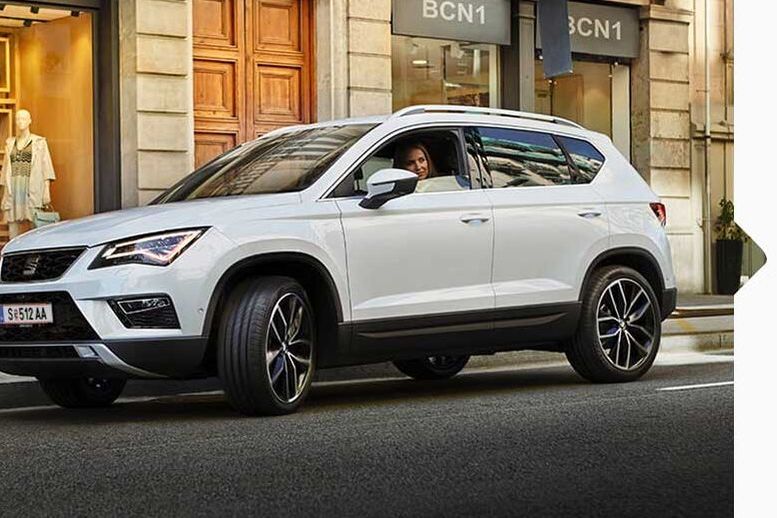 Eine Frau parkt ihren weißen SEAT Ateca 2016 am Straßenrand neben Geschäften.