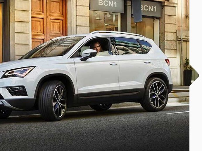 Eine Frau parkt ihren weißen SEAT Ateca 2016 am Straßenrand neben Geschäften.