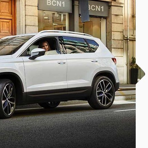 Eine Frau parkt ihren weißen SEAT Ateca 2016 am Straßenrand neben Geschäften.
