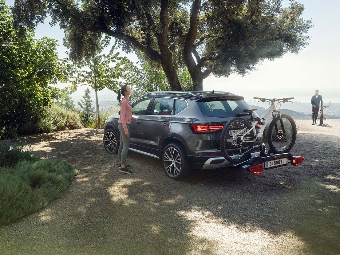Frau steht neben SEAT Ateca mit Fahrradanhänger und Mann mit Rad im Hintergrund