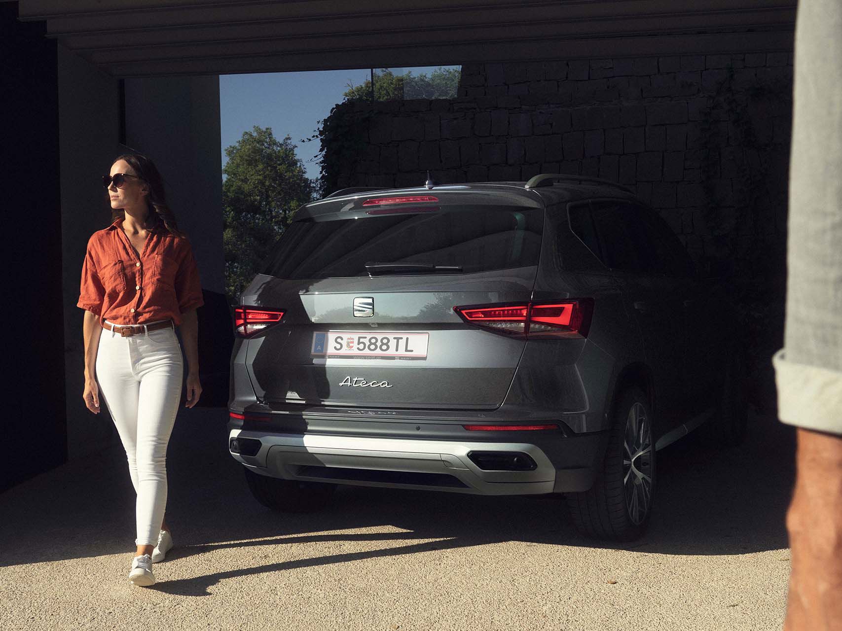 Heckansicht eines grauen SEAT Ateca in einer Garage. Eine Frau geht von dem Fahrzeug fort.