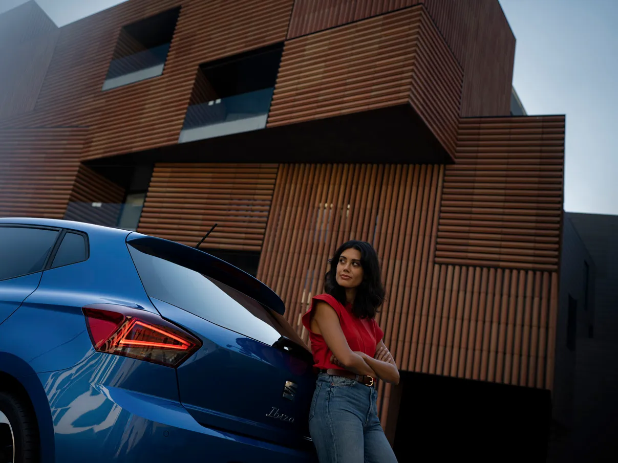 Eine Frau steht am hinteren Ende des blauen SEAT Ibiza und lehnt sich an das Heck