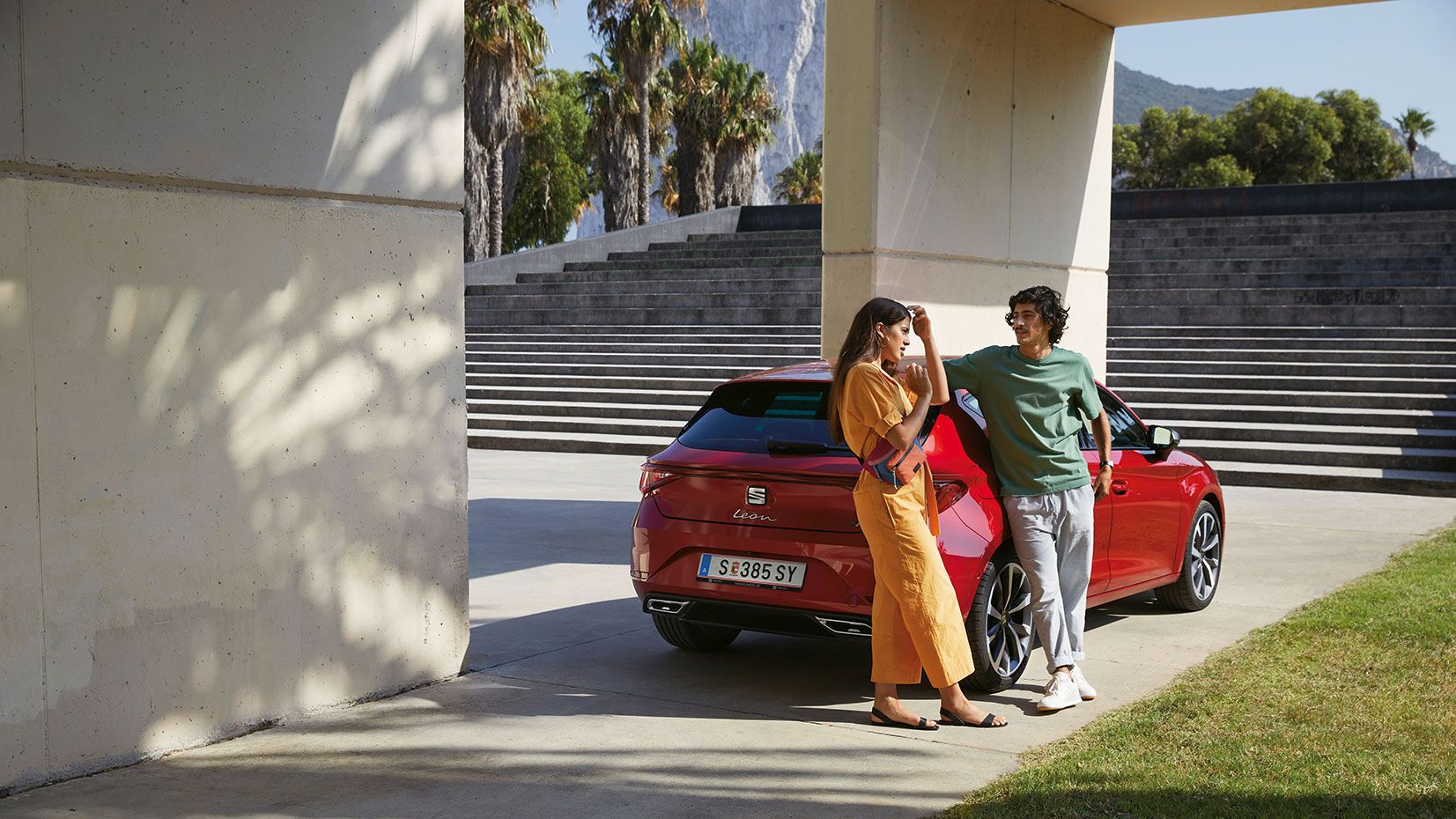 Ein Paar steht vor einem geparkten, roten SEAT Leon und unterhält sich 