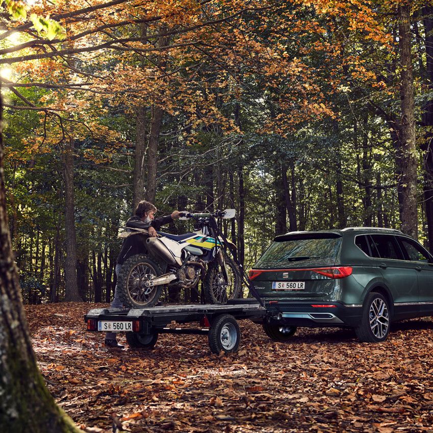 Ein Mann stellt ein Motorrad auf den Anhänger eines grünen SEAT Tarraco.