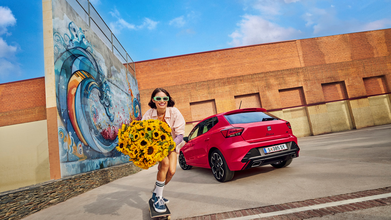 SEAT Ibize geparkt mit Mädchen auf Skateboard und Sonnenblumenstrauß daneben