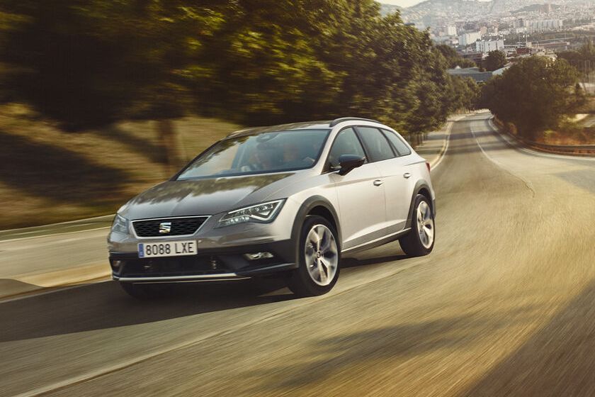 SEAT Leon fährt auf einer leeren Straße zwischen Bäumen und Feldern.