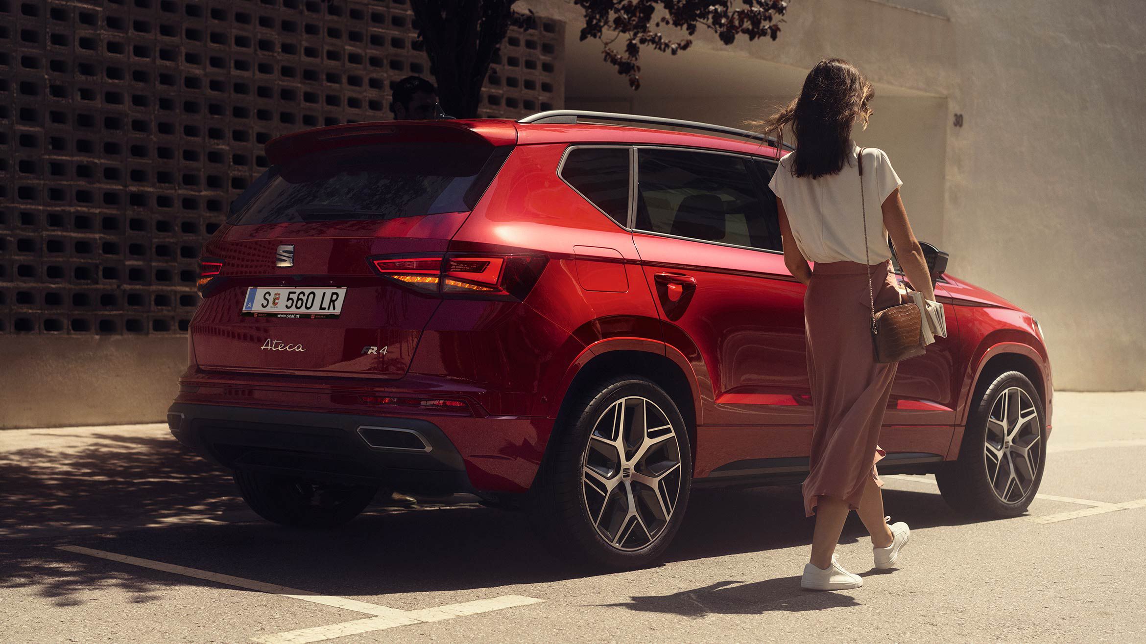 Eine Frau geht an einem roten SEAT Ateca vorbei, der am Straßenrand parkt.