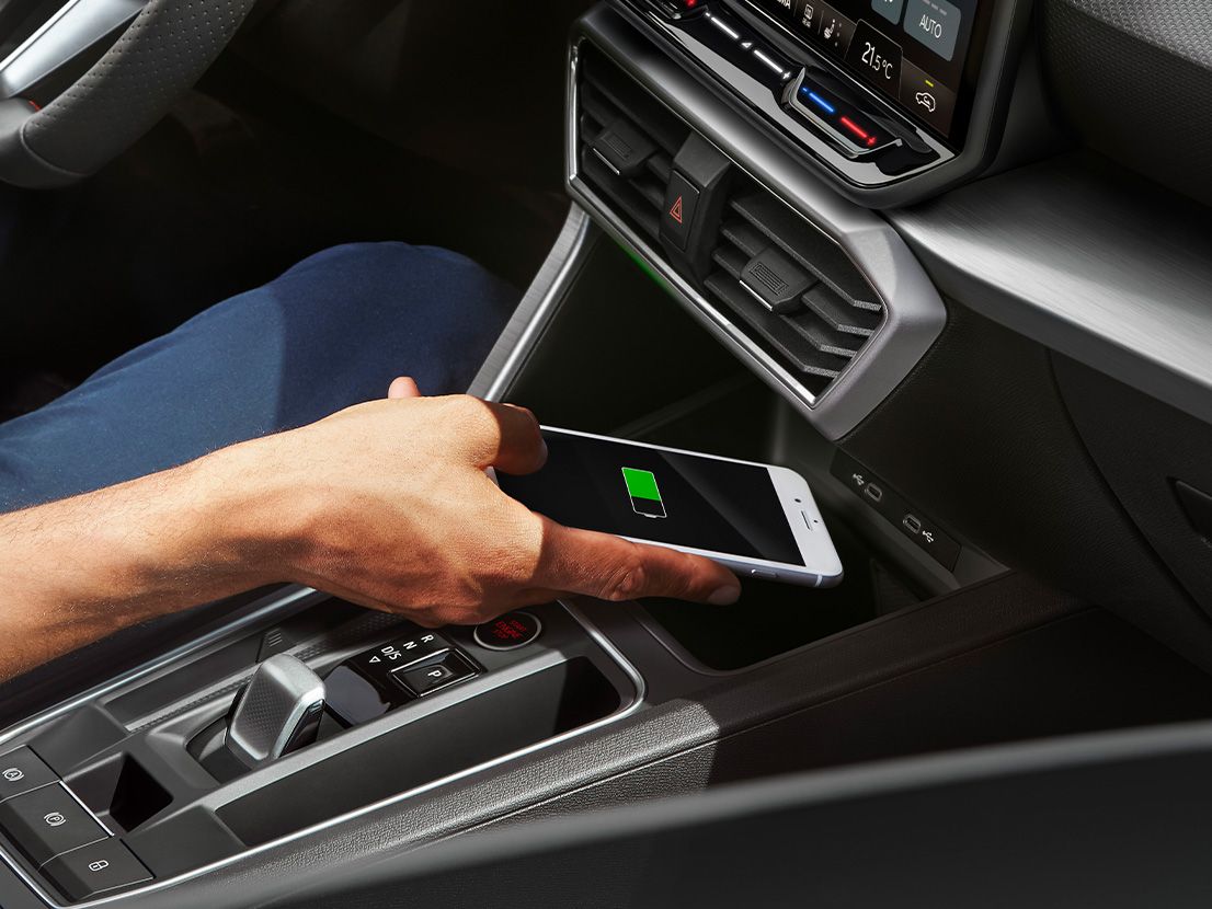 Detailansicht der Induktionsschale zum kabellosen Laden eines Smartphones im SEAT Leon 5-Türer und SEAT Leon SP Kombi. Eine Person legt gerade ein Smartphone zum Laden hinein.