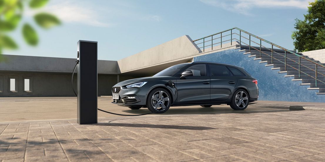 Ein grauer SEAT Leon SP Kombi wird an einer Ladesäule geladen. Im Hintergrund ist eine Treppe zu sehen.