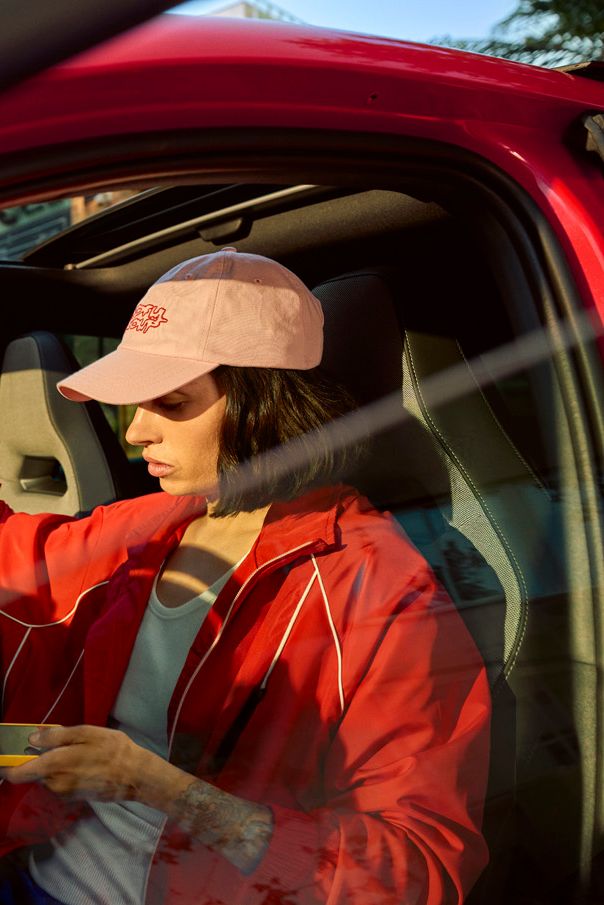 Eine Person in roter Jacke und rosa Mütze sitzt in einem roten SEAT und hält ein gelbes Smartphone. Sie zeigt mit einer Hand nach oben.