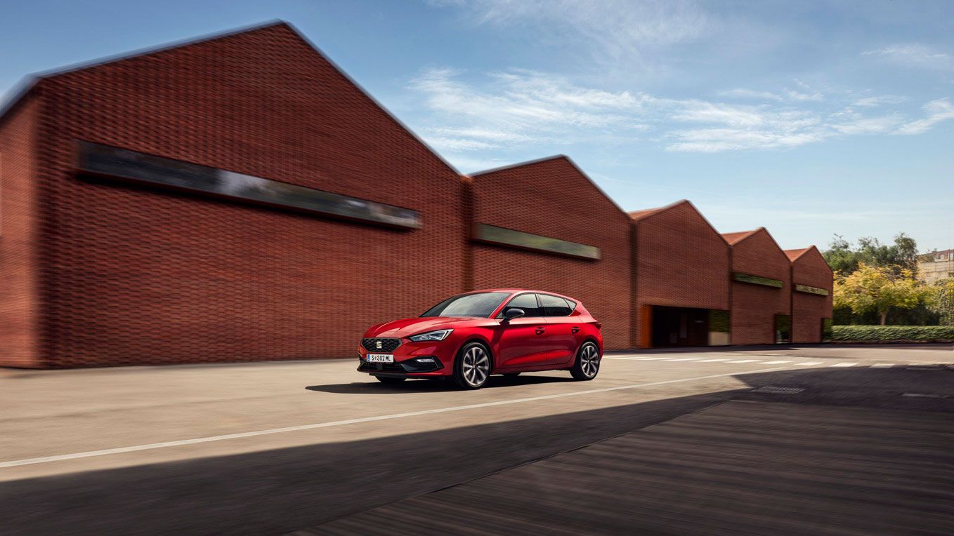 Ein roter SEAT Leon 5-Türer in Bewegung vor einem industriellen Hintergrund.