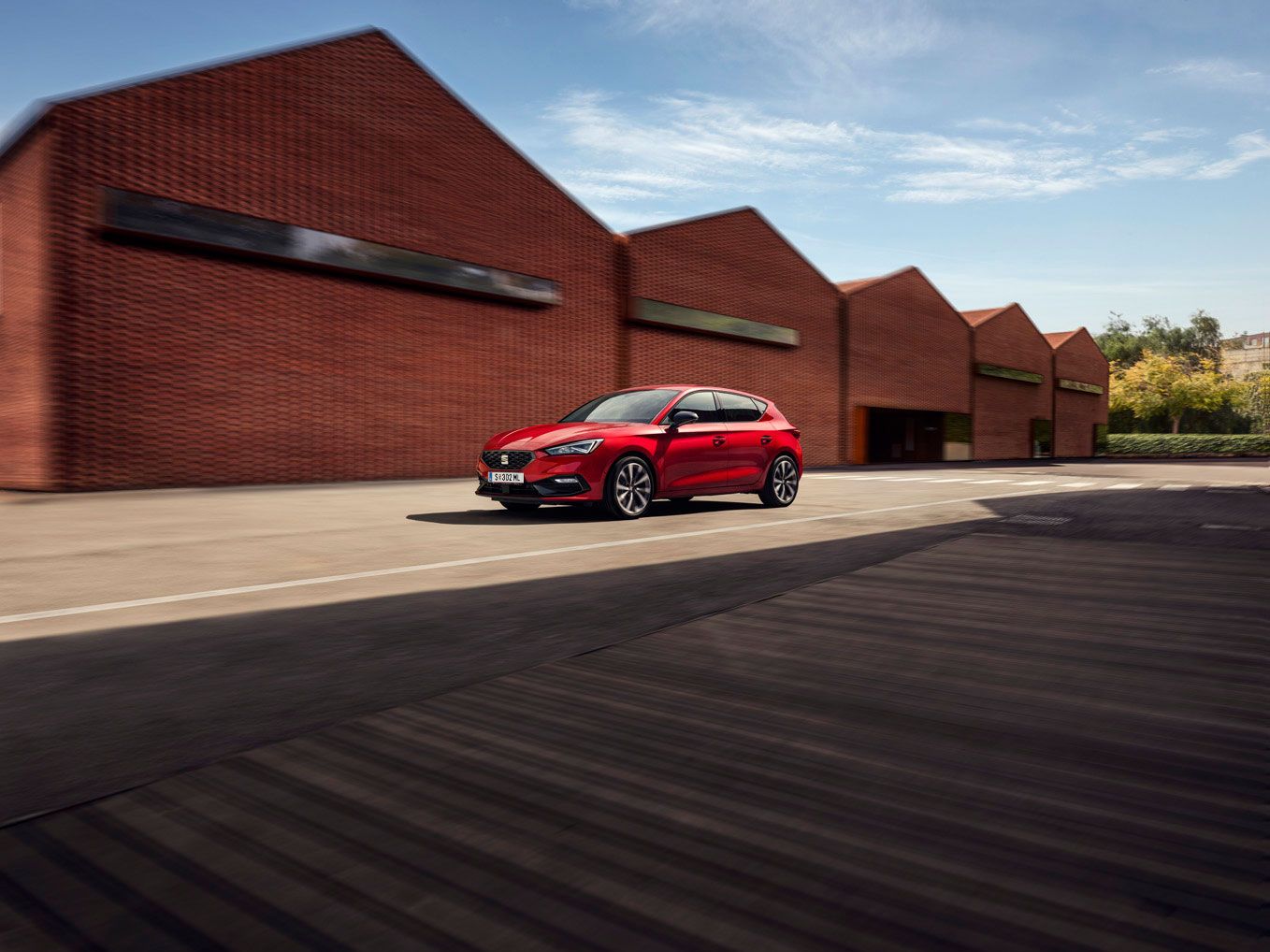 Ein roter SEAT Leon 5-Türer in Bewegung vor einem industriellen Hintergrund.