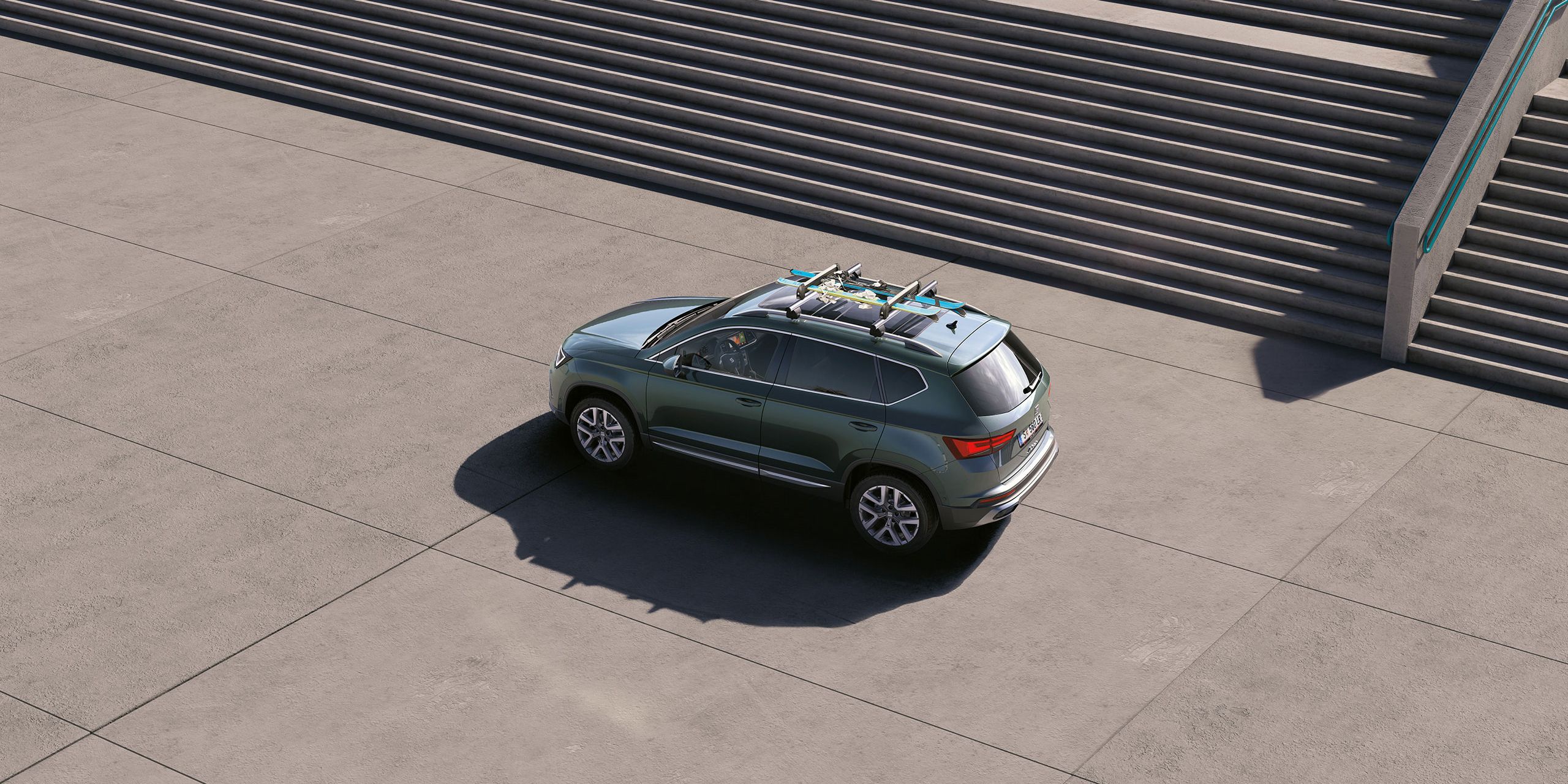 Ein grüner SEAT Ateca mit Dachträger und darauf montierten Skiern.
