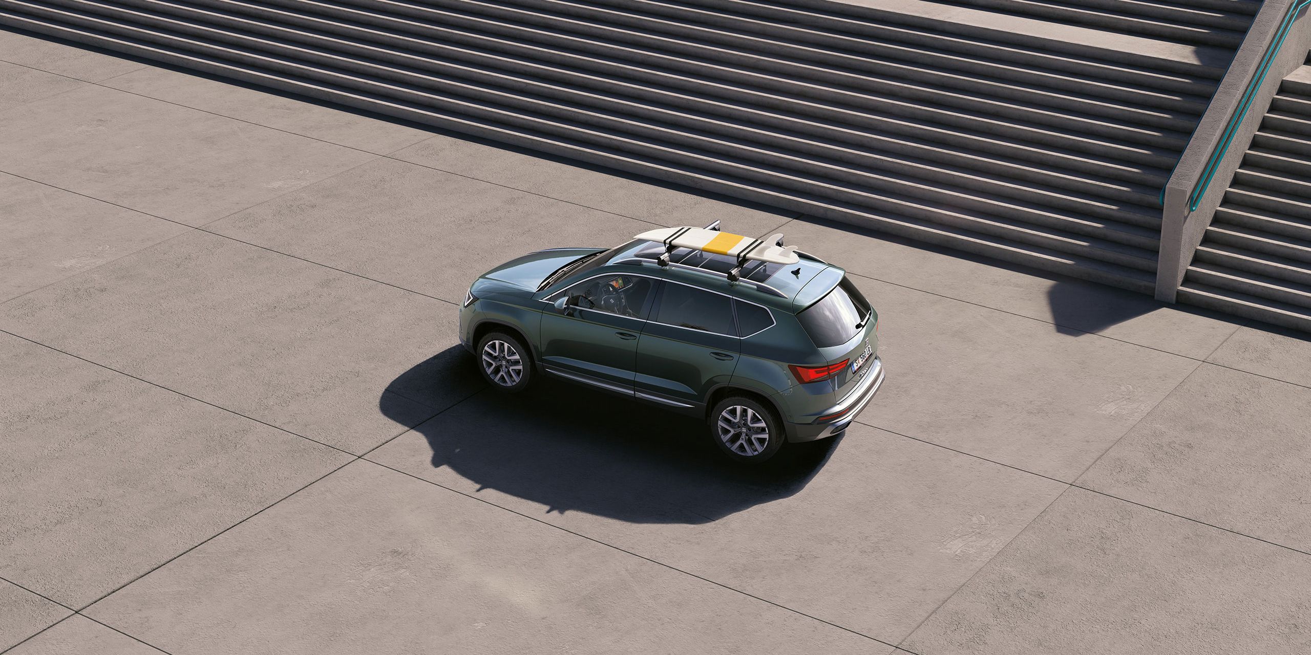 Ein grüner SEAT Ateca mit Dachträger und einem Surfbrett auf dem Dach.