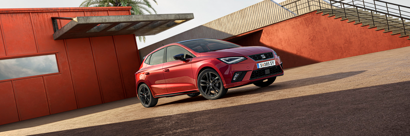 Schräge Frontansicht eines roten SEAT Ibiza vor einem Gebäude und einer Treppe rechts davon.