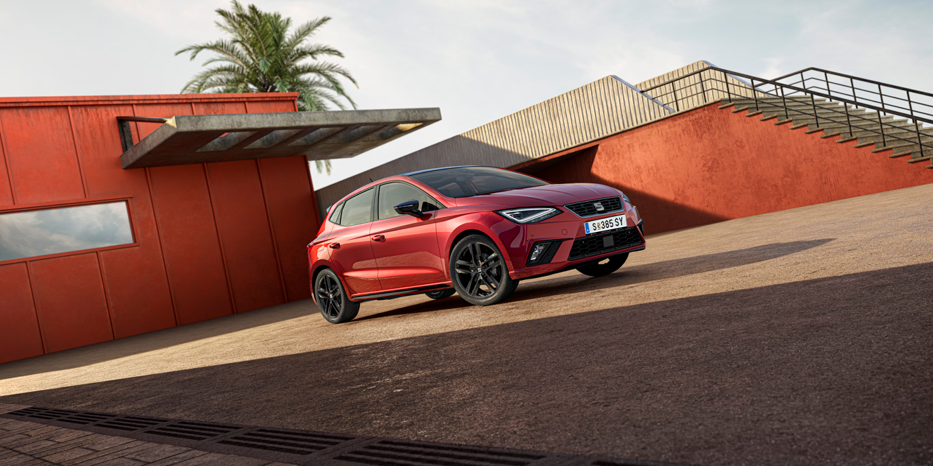 Schräge Frontansicht eines roten SEAT Ibiza vor einem Gebäude und einer Treppe rechts davon.