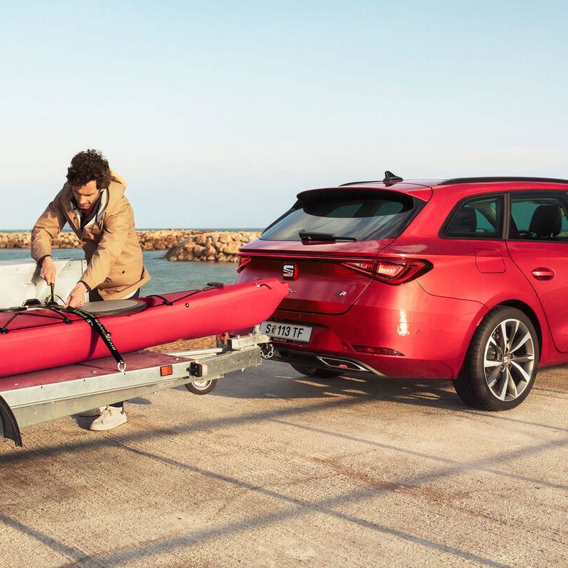 Ein roter SEAT Leon SP Kombi mit Anhänger an der Küste. Ein Mann montiert ein Kanu auf dem Anhänger.