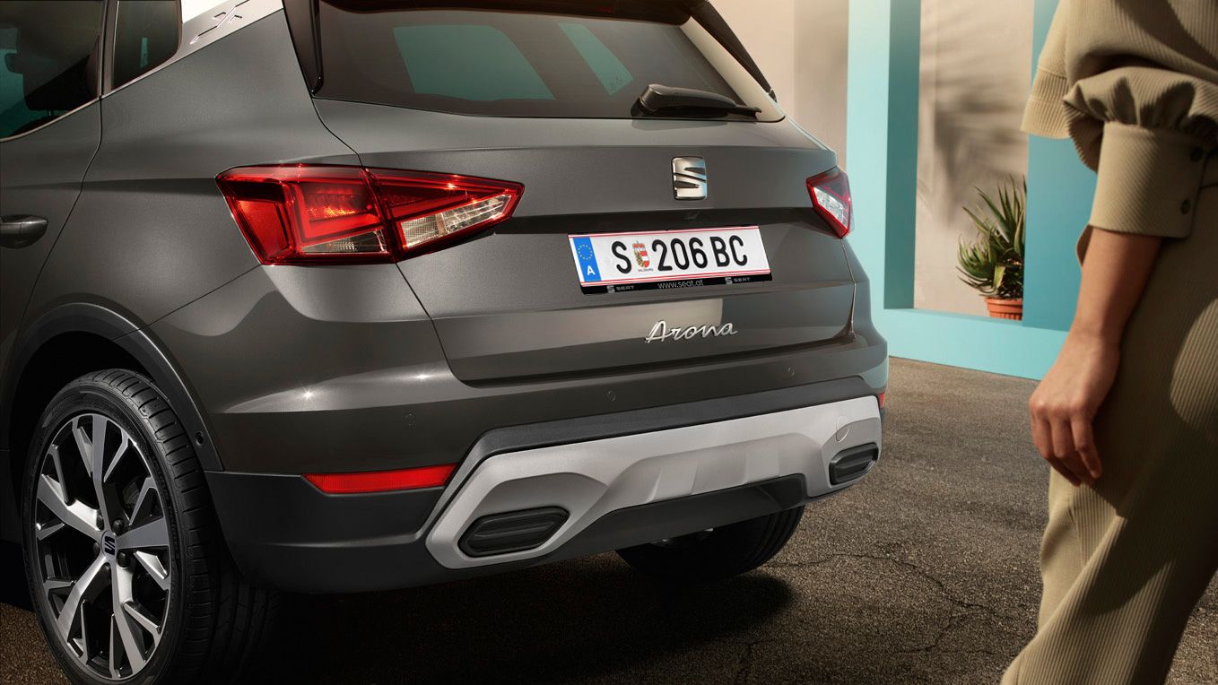 Eine Frau geht in Richtung eines SEAT Arona (Heckansicht) 