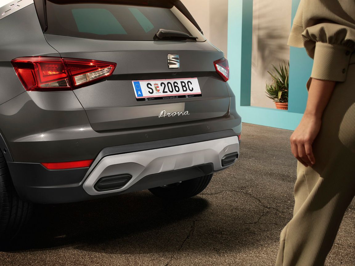 Eine Frau geht in Richtung eines SEAT Arona (Heckansicht) 