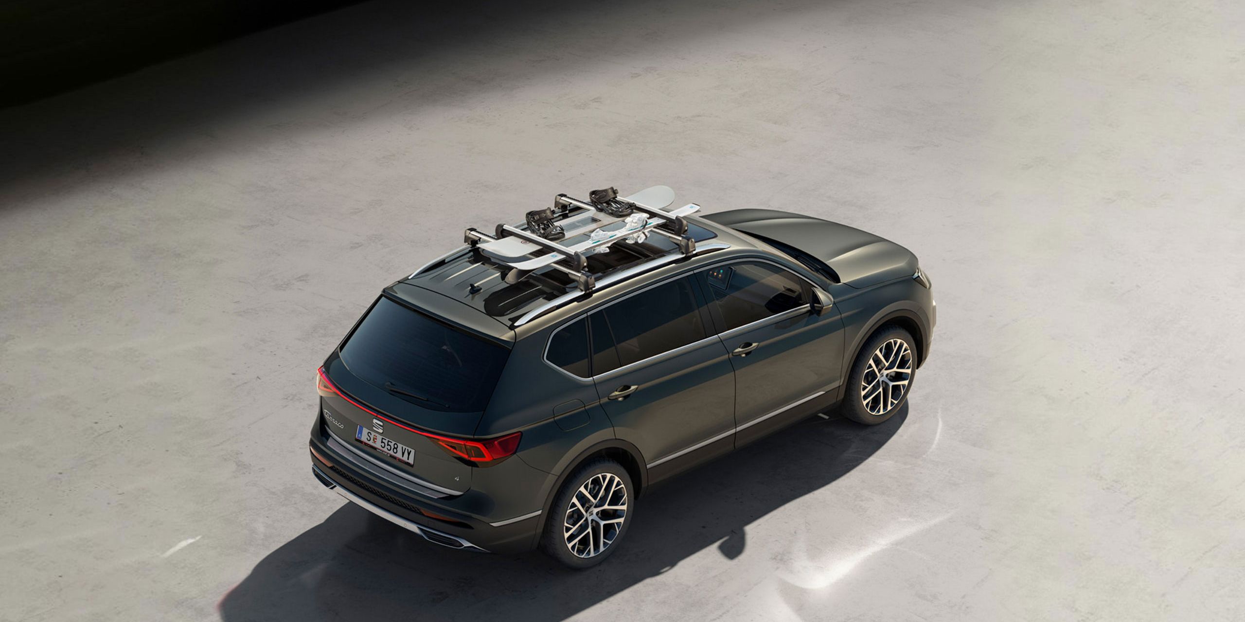 Ein grüner SEAT Tarraco mit Dachträger auf dem ein Snowboard und ein Paar Ski montiert sind.