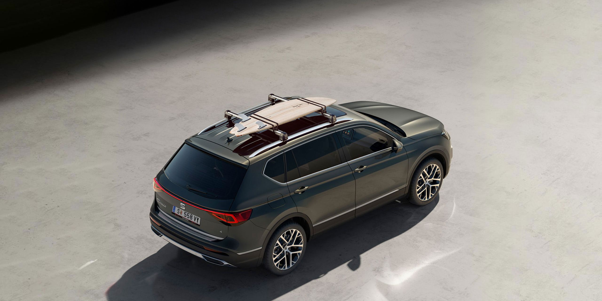 Ein grüner SEAT Tarraco mit Dachträger auf dem ein Surfbrett montiert ist.