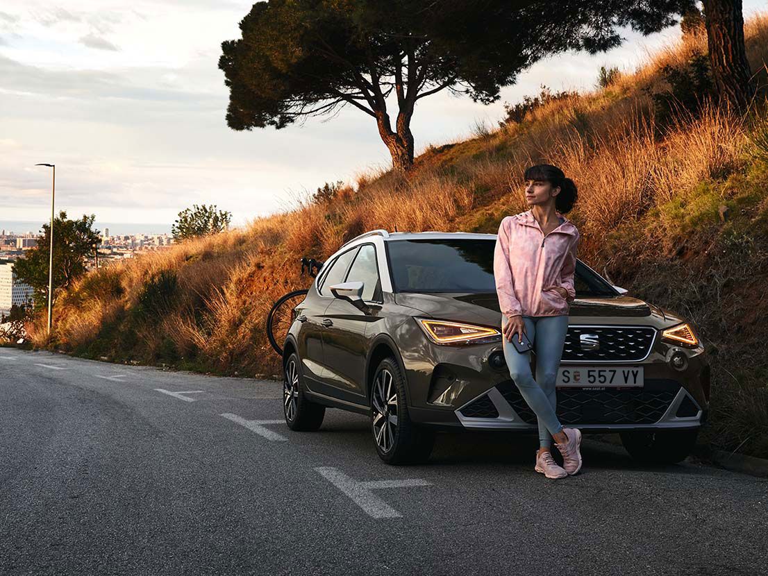 Eine Frau lehnt an der Motorhaube eines SEAT Arona.