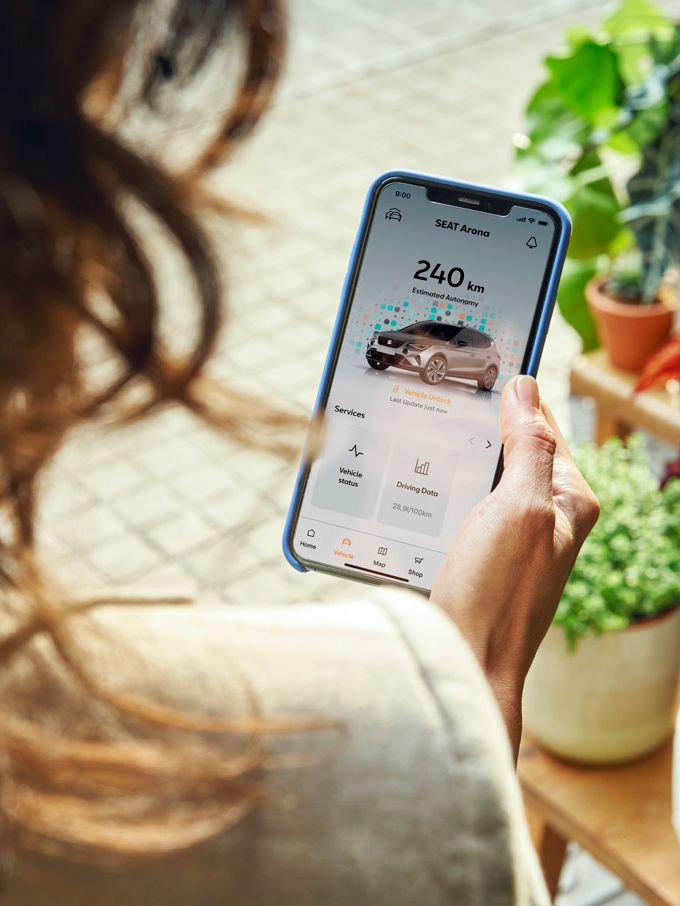 Eine Frau schaut auf ihr Smartphone und checkt die Reichweite von ihrem SEAT Arona.