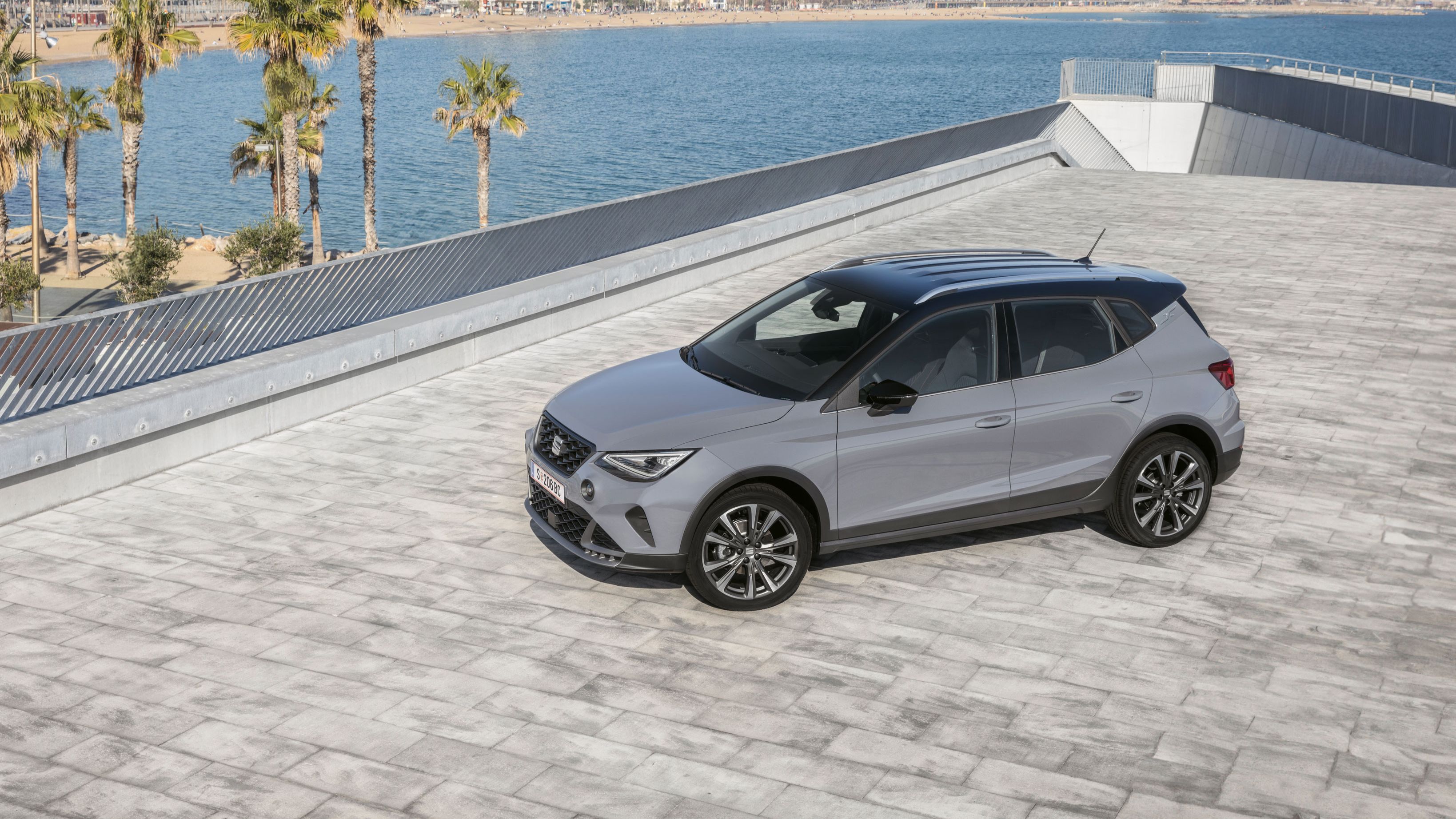 SEAT Arona FR Modelle in Hellgrau stehen aus schräger Perspektive im Vordergrund, während im Hintergrund ein Hafen zu erkennen ist