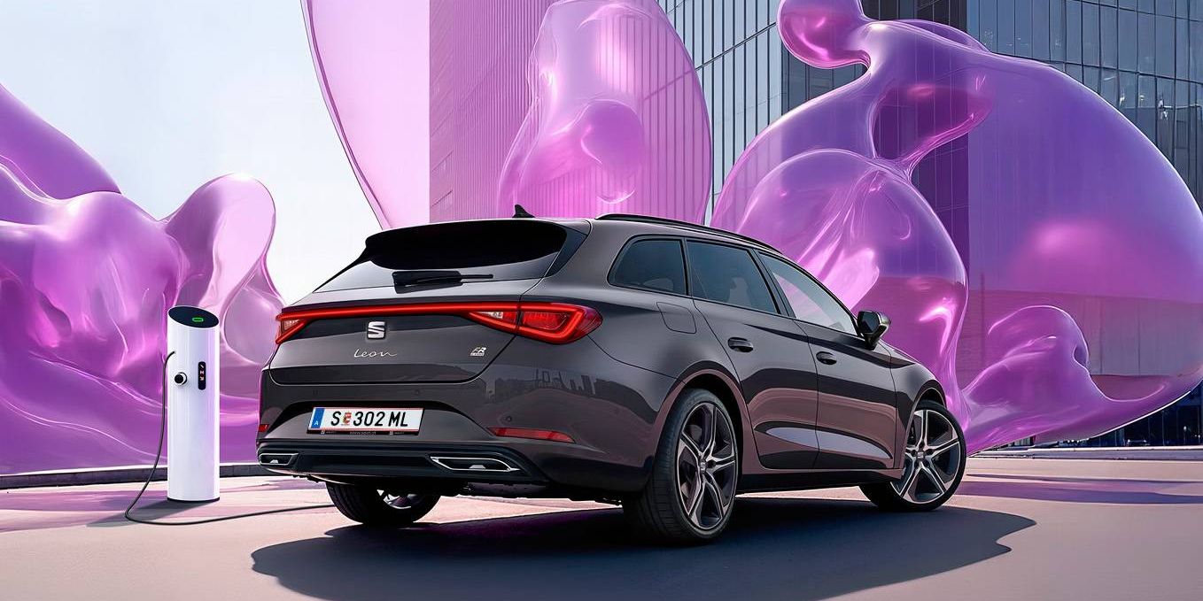 Schräge Heckansicht eines dunkelgrauen SEAT Leon SP Kombi beim Laden an einer Ladesäule vor einem modernen Gebäude mit Glasfronten.