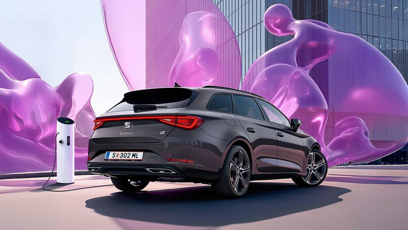 Schräge Heckansicht eines dunkelgrauen SEAT Leon SP Kombi beim Laden an einer Ladesäule vor einem modernen Gebäude mit Glasfronten.