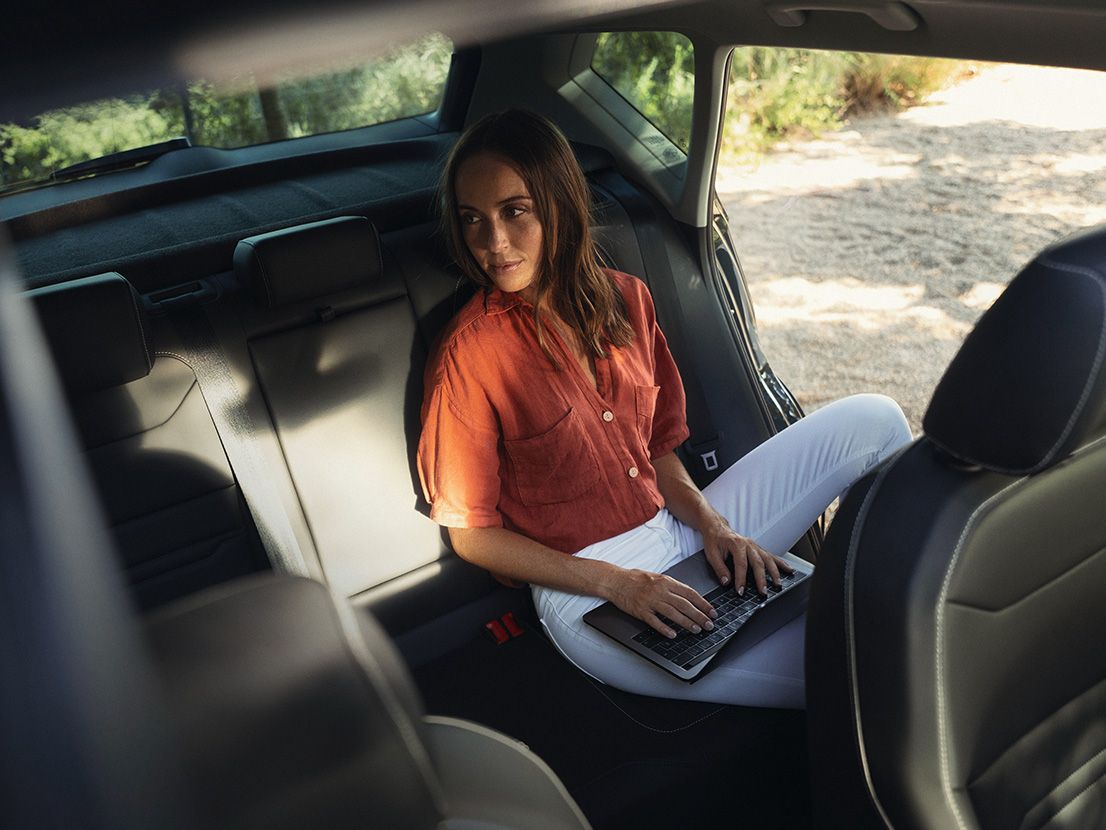 Eine Frau mit Laptop auf dem Schoß sitzt am Rücksitz eines SEAT Ateca.
