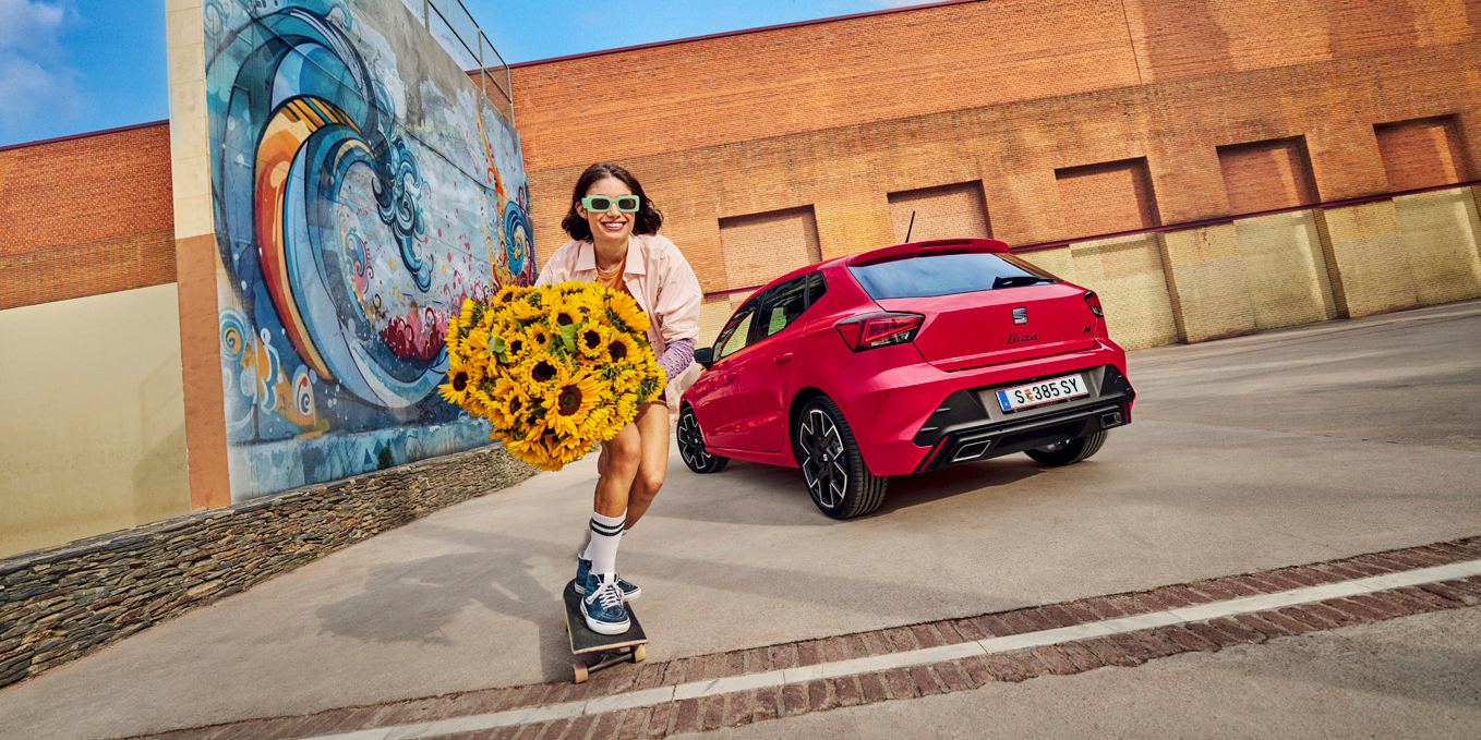 SEAT Ibize geparkt mit Mädchen auf Skateboard und Sonnenblumenstrauß daneben