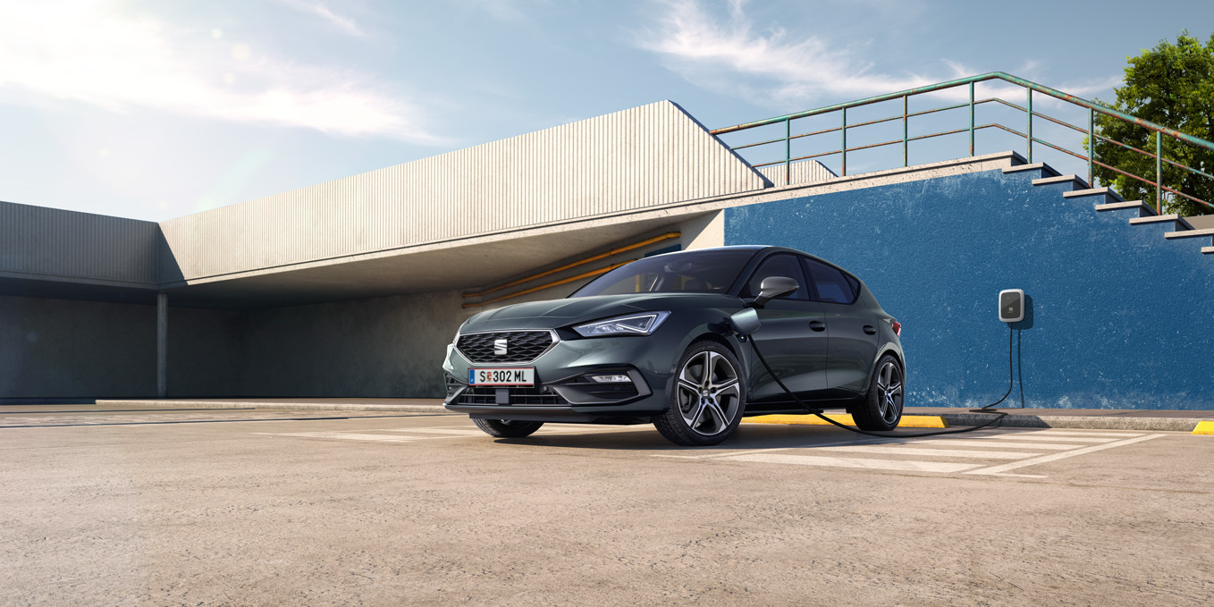 Ein grauer SEAT Leon e-Hybrid vor einem Gebäude mit einer Treppe beim Ladevorgang.