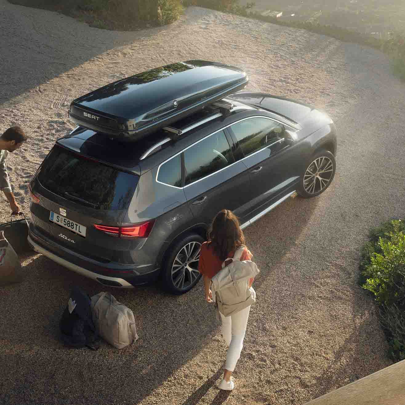 Ein graphitegrauer SEAT Ateca mit Dachbox – ein Paar packt ein und macht sich bereit für den nächsten Trip