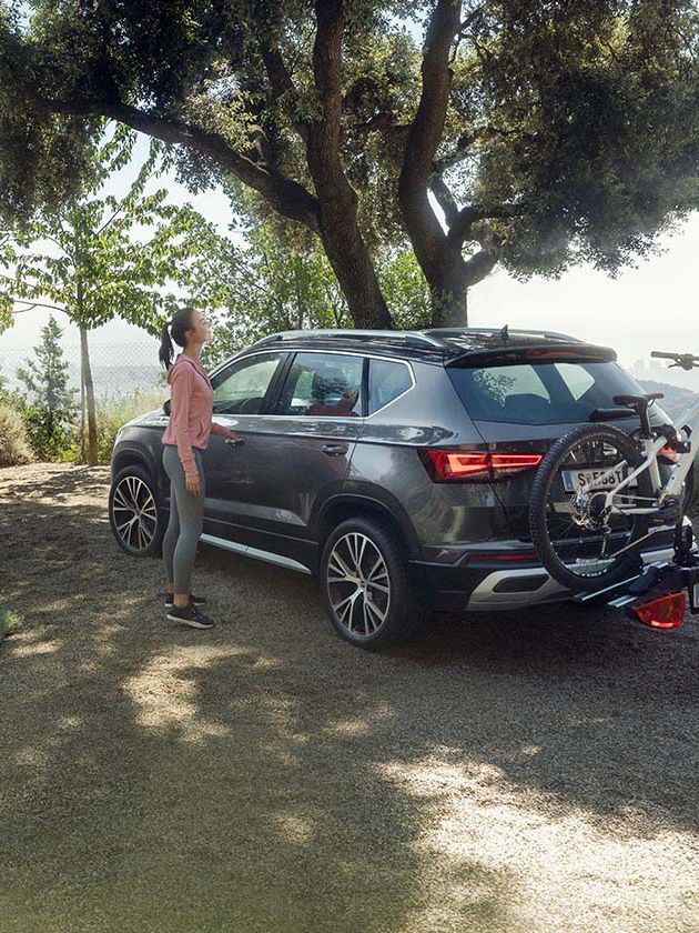 Frau steht neben SEAT Ateca mit Fahrradanhänger und Mann mit Rad im Hintergrund