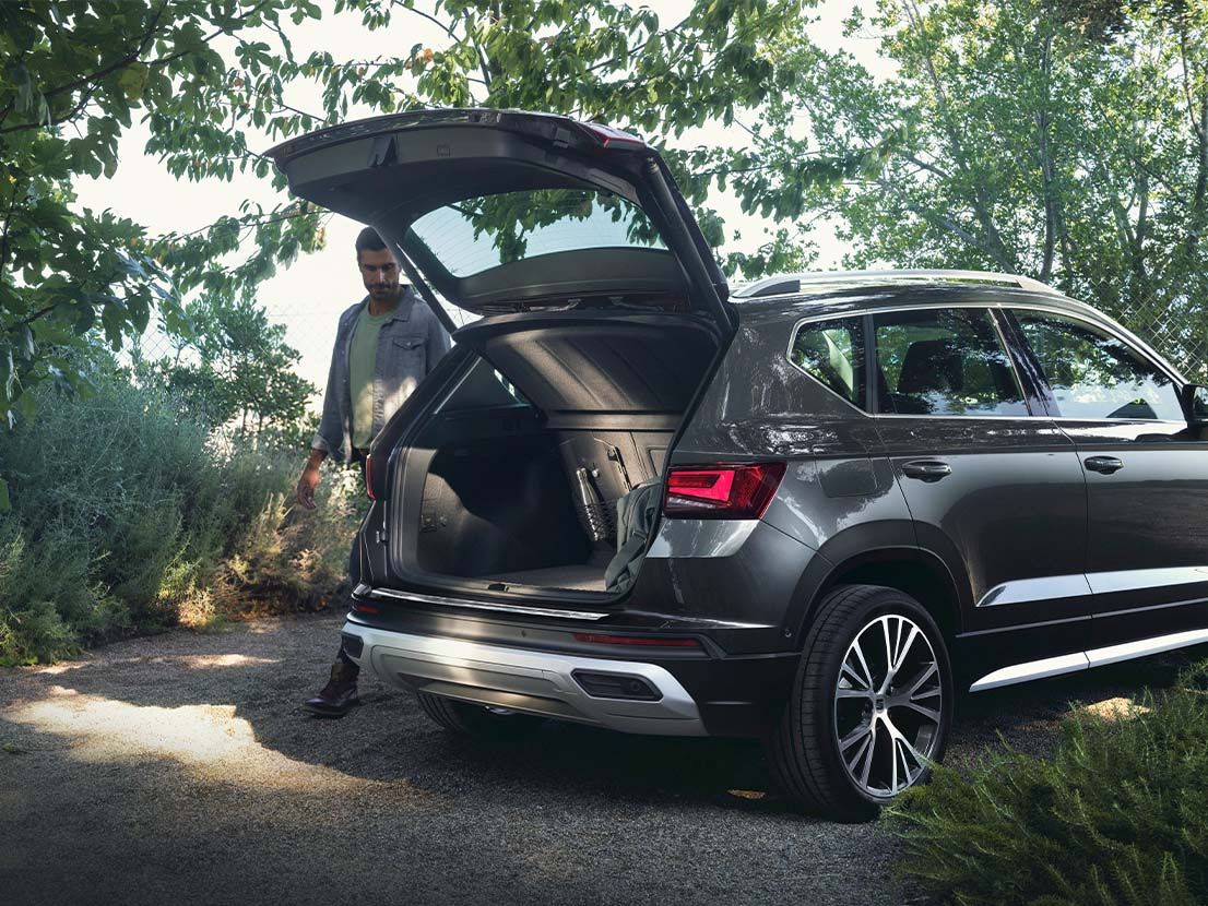 Ein Mann steht neben einem grauen SEAT Ateca mit geöffnetem Kofferraum.