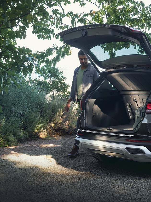Ein Mann steht neben einem grauen SEAT Ateca mit geöffnetem Kofferraum.