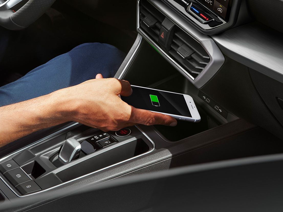 Detailansicht der Induktionsschale zum kabellosen Laden eines Smartphones im SEAT Leon SP Kombi. Eine Person legt gerade ein Smartphone zum Laden hinein.