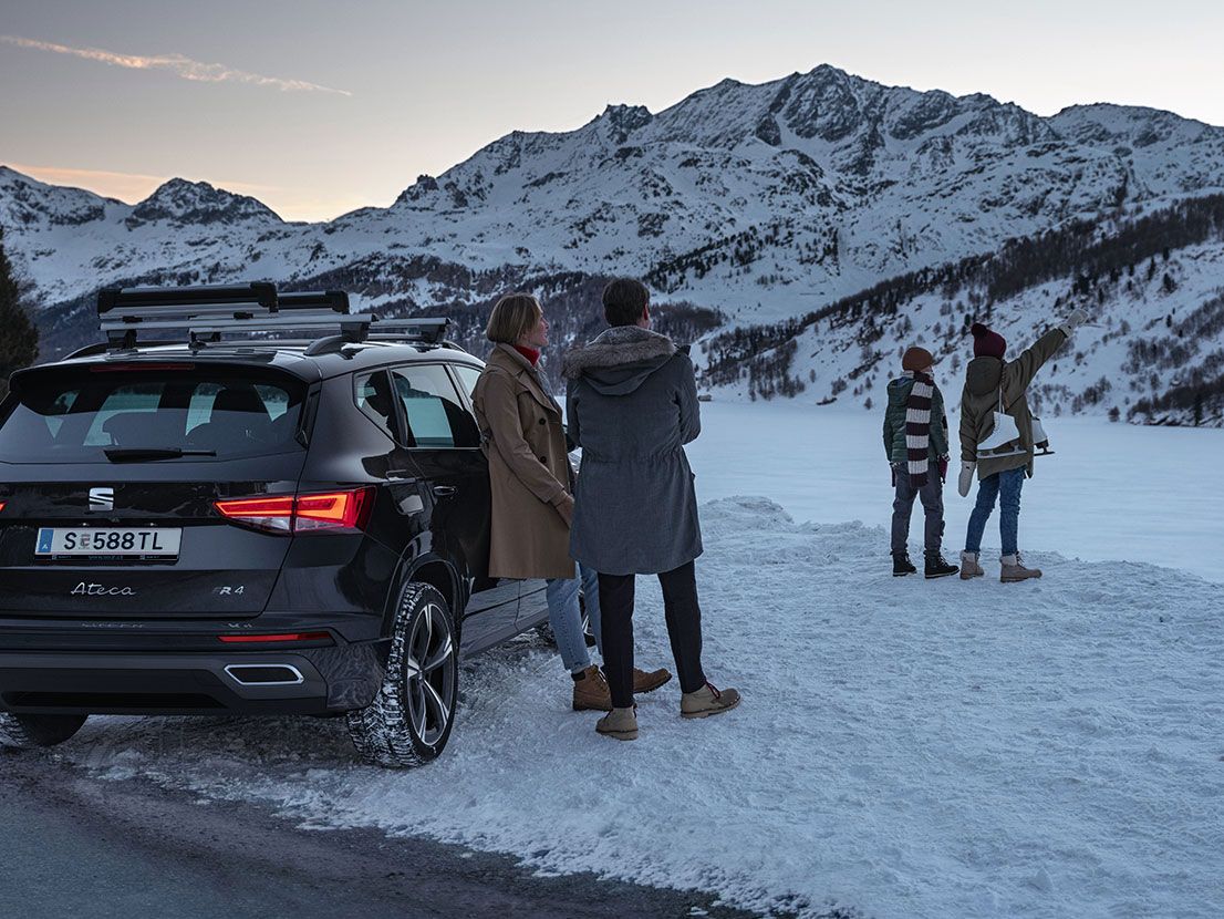 Eine Familie parkt mit ihrem schwarzen SEAT Ateca an einem zugefrorenen See in den winterlichen Bergen.