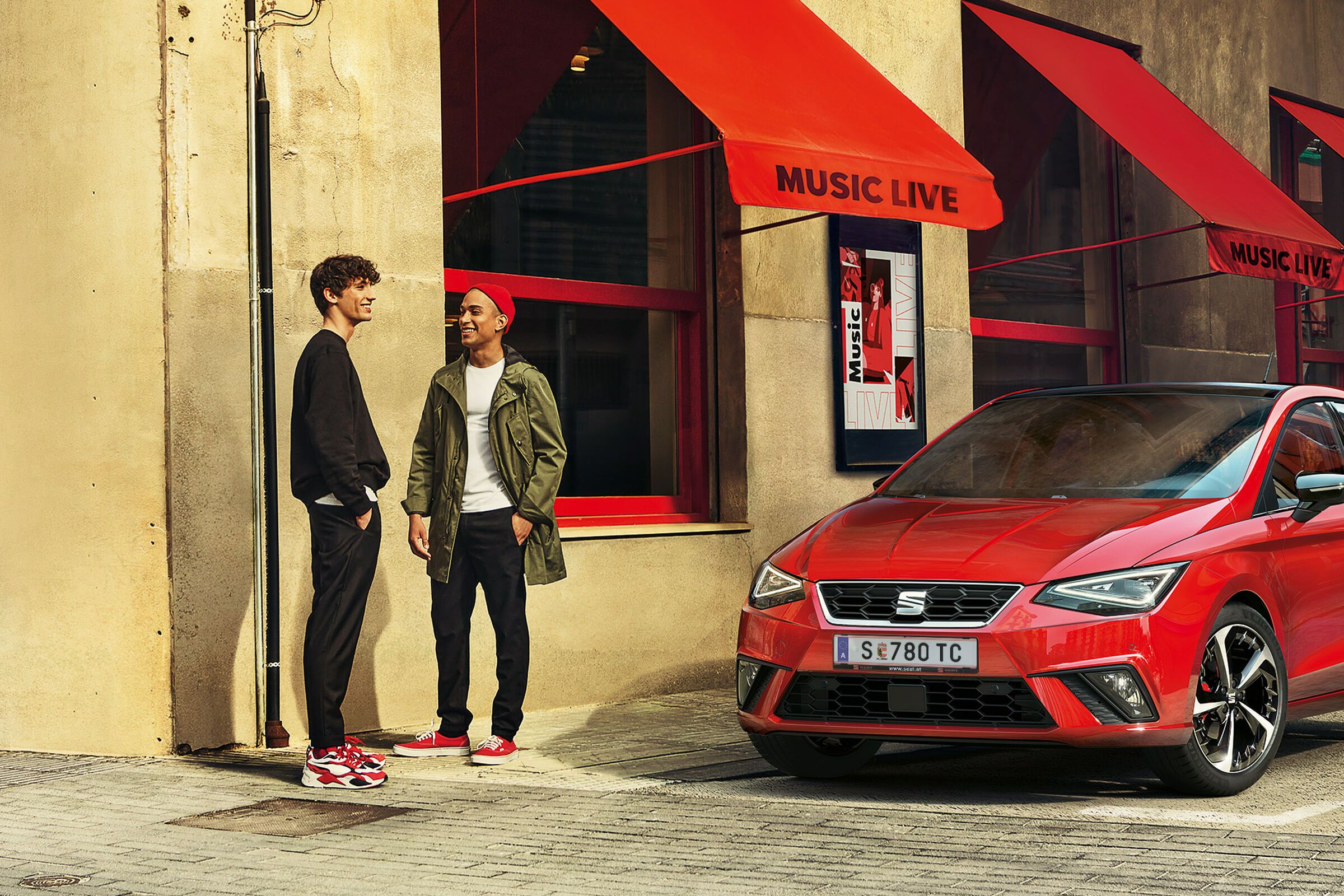 Ein roter SEAT Ibiza steht vor einem Gebäude während zwei Männer davor reden