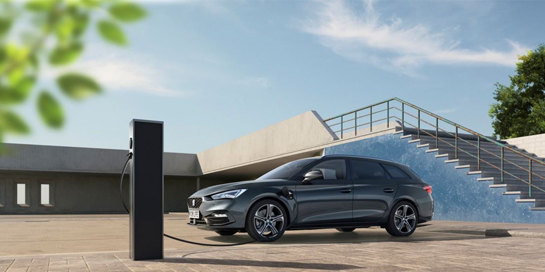 Ein grauer SEAT Leon SP Kombi wird an einer Ladesäule geladen. Im Hintergrund ist eine Treppe zu sehen.