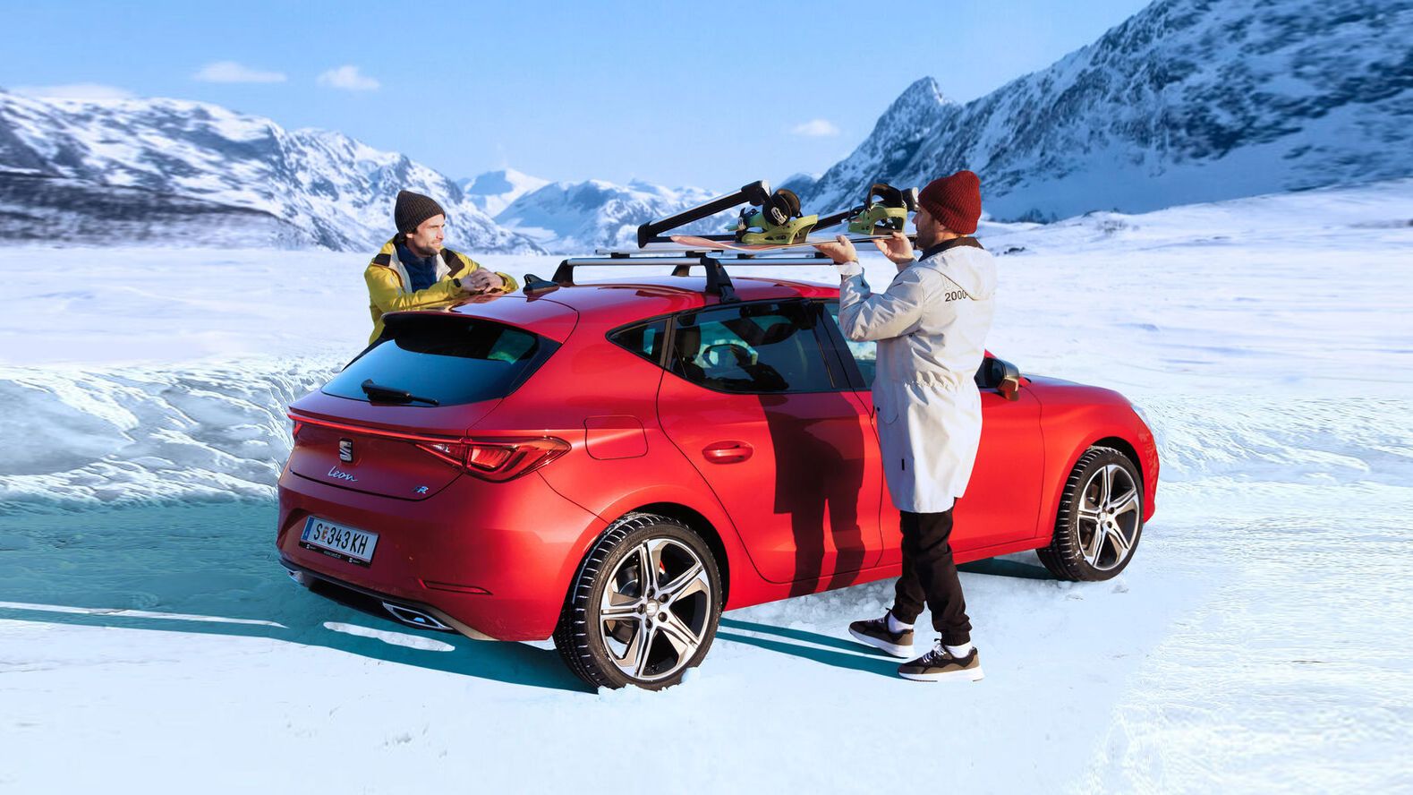 Ein roter SEAT Leon steht auf einer verschneiten Fahrbahn, während zwei Personen gerade Dachträger am Fahrzeug montieren.